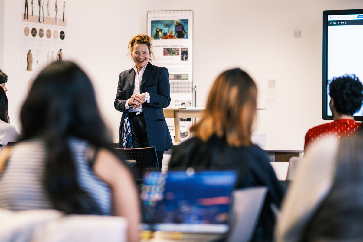 A lecturer standing in front of a small seminar group, there are 2 people in the foreground on laptops.
