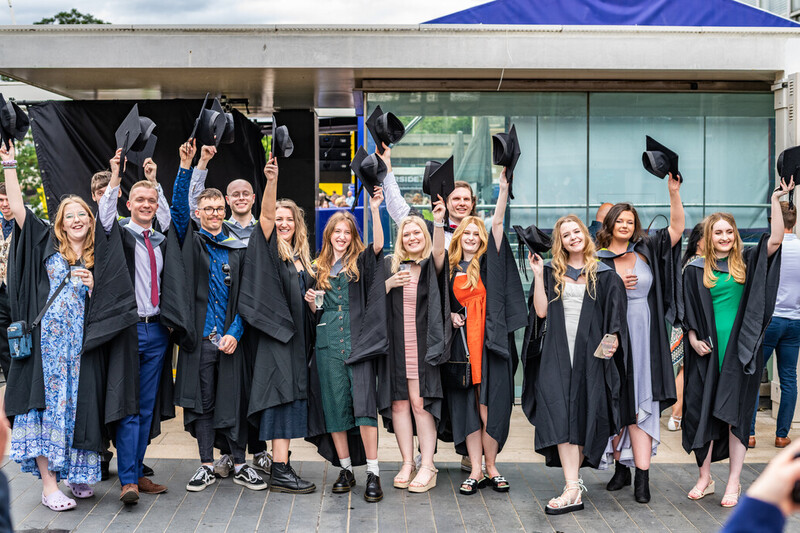 a large group of students throw their caps in the air for graduation 2022